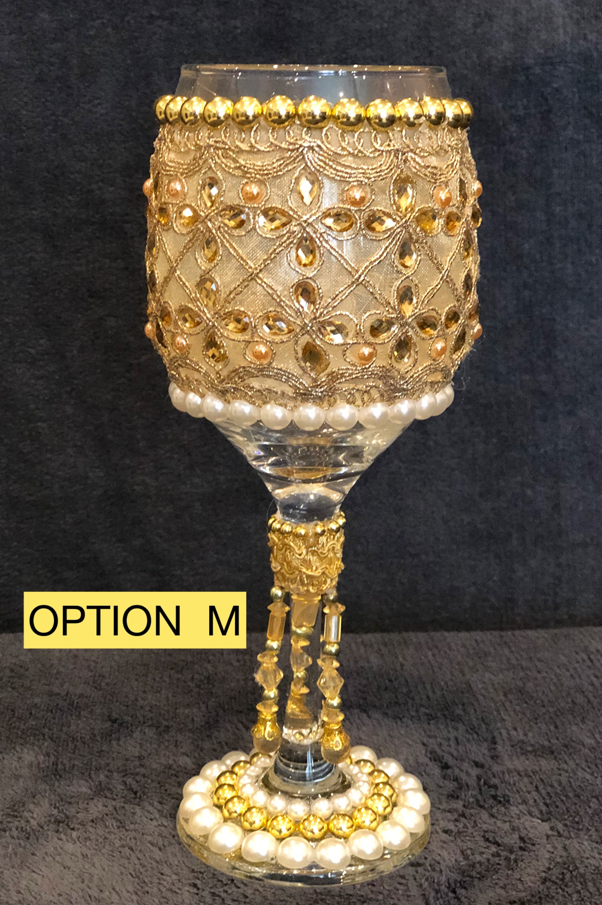 Decorative wine glass with gold and pearl embellishments on a black background